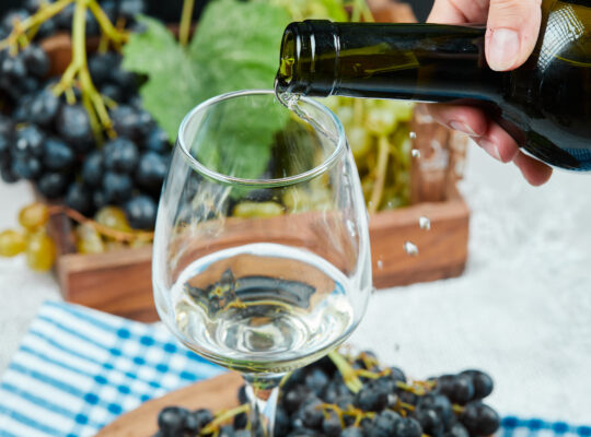 Pouring wine into the glass with plate of grapes on white table. High quality photo